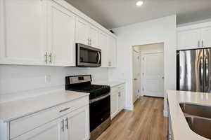 Kitchen featuring stainless steel appliances, white cabinets, light wood-style flooring, recessed lighting, and light stone counters