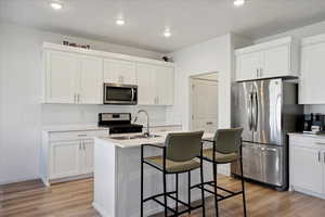 Kitchen with white cabinets, stainless steel appliances, light wood-style flooring, recessed lighting, and a kitchen island with sink