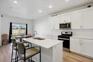 Kitchen with appliances with stainless steel finishes, white cabinets, light wood-style floors, a center island with sink, and recessed lighting