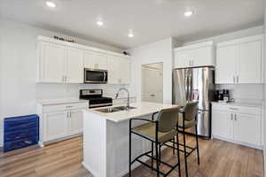 Kitchen featuring appliances with stainless steel finishes, light wood finished floors, white cabinets, a breakfast bar area, and recessed lighting