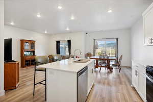 Kitchen with dishwasher, light wood-style flooring, light countertops, white cabinets, and recessed lighting