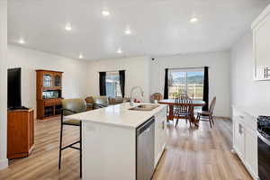 Kitchen with white cabinetry, a center island with sink, dishwasher, a kitchen bar, and light wood-type flooring