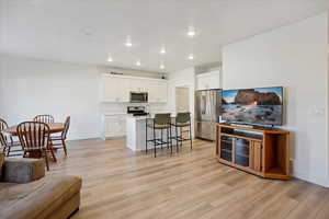 Kitchen with a breakfast bar, white cabinets, light wood-style flooring, stainless steel appliances, and a kitchen island with sink