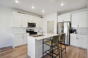Kitchen with stainless steel appliances, white cabinets, light wood-style floors, a kitchen breakfast bar, and recessed lighting