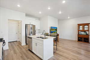 Kitchen with white cabinets, recessed lighting, a kitchen bar, light wood finished floors, and a center island with sink