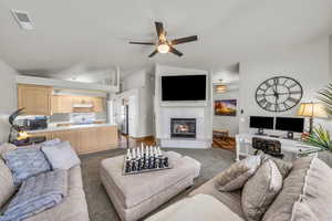 Living area featuring carpet flooring, a ceiling fan, a tiled fireplace, and lofted ceiling