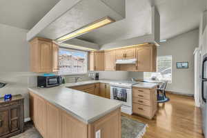 Kitchen with white range with electric stovetop, light brown cabinets, under cabinet range hood, and a peninsula