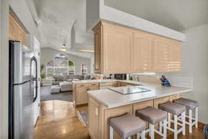Kitchen featuring freestanding refrigerator, light brown cabinetry, a peninsula, electric cooktop, and light wood finished floors