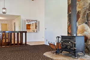 Living area with a wood stove, carpet floors, and a towering ceiling