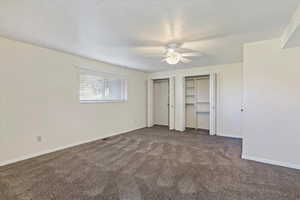 Unfurnished bedroom featuring multiple closets, carpet, a ceiling fan, and a textured ceiling