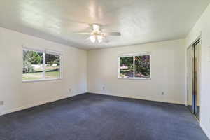 Unfurnished bedroom featuring multiple windows, a textured ceiling, dark colored carpet, and ceiling fan
