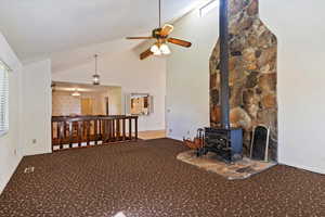 Carpeted living room featuring a wood stove, a ceiling fan, and high vaulted ceiling