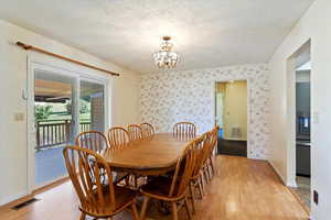 Dining room featuring light wood-style flooring, a chandelier, a textured ceiling, and wallpapered walls