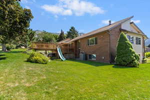 Rear view of property with a deck with mountain view, brick siding, and a yard