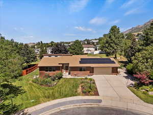 View of front featuring driveway, solar panels, an attached garage, and a shingled roof