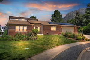 View of front featuring brick siding, solar panels, and a front yard