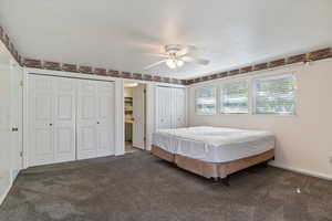 Bedroom with two closets, carpet, ceiling fan, and a textured ceiling