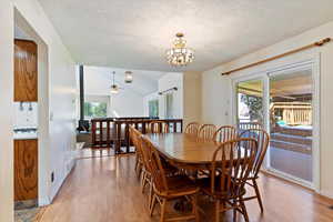 Dining space with light wood finished floors, a textured ceiling, a chandelier, ceiling fan, and lofted ceiling