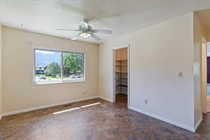 Unfurnished bedroom featuring a walk in closet, a textured ceiling, and ceiling fan