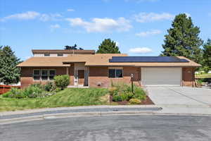Single story home featuring driveway, brick siding, solar panels, and a garage