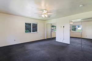 Unfurnished bedroom featuring multiple closets, multiple windows, dark colored carpet, and ceiling fan