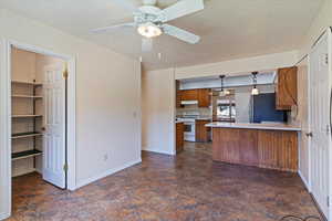 Kitchen with white gas range oven, brown cabinets, freestanding refrigerator, light countertops, and a peninsula