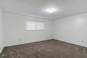 Empty room with dark carpet and a textured ceiling