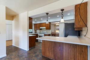 Kitchen with white gas range oven, freestanding refrigerator, a peninsula, light countertops, and recessed lighting