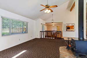Carpeted empty room with a wood stove, ceiling fan, and high vaulted ceiling