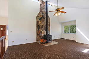 Unfurnished living room featuring a wood stove, high vaulted ceiling, carpet floors, and a ceiling fan