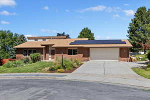 View of front of house featuring brick siding, an attached garage, concrete driveway, roof mounted solar panels, and a front lawn