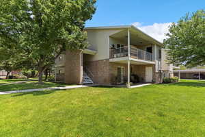 View of property with a balcony, brick siding, a yard, and a patio