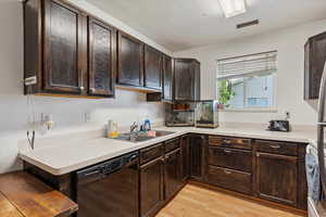 Kitchen with dishwasher, dark brown cabinets, light wood finished floors, and light countertops