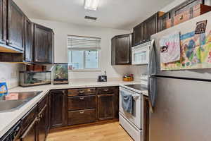 Kitchen with white appliances, dark brown cabinets, light wood-type flooring, and light countertops