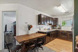 Kitchen with black dishwasher, light wood-style flooring, dark brown cabinets, and light countertops