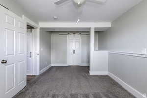 Unfurnished bedroom with a barn door, carpet floors, a textured ceiling, a closet, and a ceiling fan