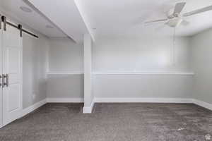 Carpeted empty room featuring a barn door and a ceiling fan