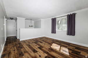 Empty room with a chandelier, dark wood-style flooring, and ornamental molding