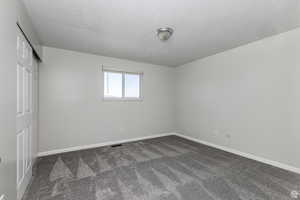 Unfurnished bedroom featuring dark colored carpet, a textured ceiling, and a closet