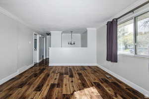 Empty room featuring a chandelier, ornamental molding, and wood finished floors