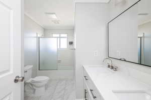 Full bath featuring crown molding, double vanity, enclosed tub / shower combo, and marble look tile flooring