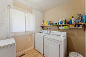 Laundry room with washing machine and dryer, wallpapered walls, and light wood-type flooring