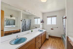 Bathroom with double vanity, wood finished floors, and shower / tub combo with curtain