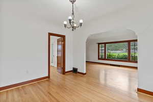 Spare room with light wood finished floors, arched walkways, and a chandelier