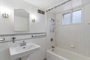 Full bathroom featuring a textured wall, shower / washtub combination, tile walls, and wainscoting