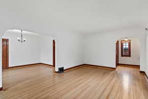 Unfurnished living room featuring arched walkways, a chandelier, and light wood-style flooring