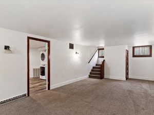 Basement with carpet flooring, stacked washing machine and dryer, and stairs