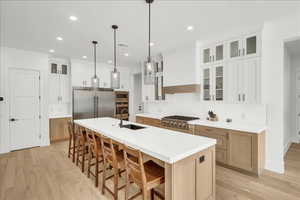 Kitchen featuring built in appliances, light wood-style flooring, a center island with sink, light countertops, and a kitchen breakfast bar