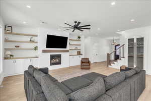 Living area with stairs, light wood-style flooring, a brick fireplace, ceiling fan, and recessed lighting