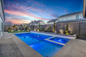 Pool at dusk with a pool with connected hot tub, a fenced backyard, and a patio